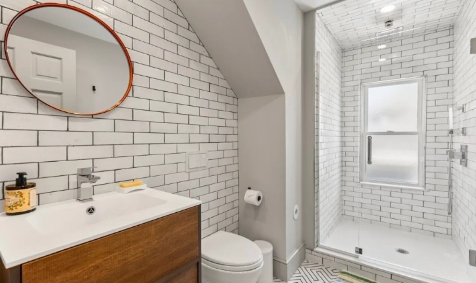 Subway-tile bathroom with a round mirror in a Beals Street condominium